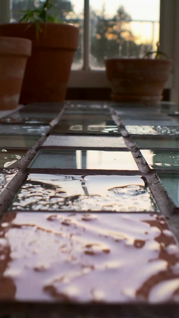 Vertikal video: Vand samler sig på mosaikfliser, spreder sig nær vinduet, spejler terrakottapotter, himmel
