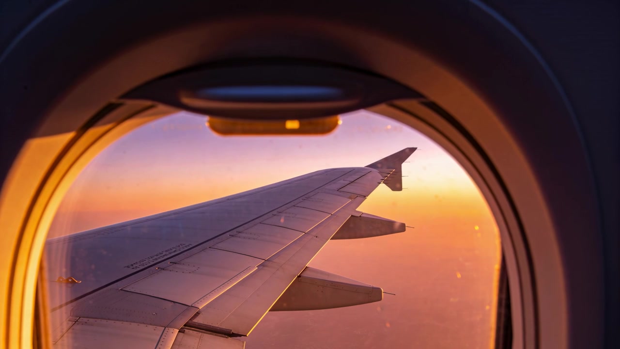 Mostrando el ala izquierda de un avión reflejando el resplandor del atardecer a través de la ventanilla de la cabina, con winglet y motas.