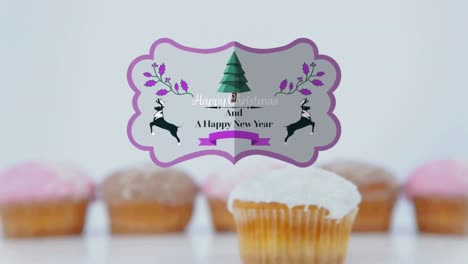 Animation-of-christmas-greetings-on-tag-over-cupcakes-on-white-background