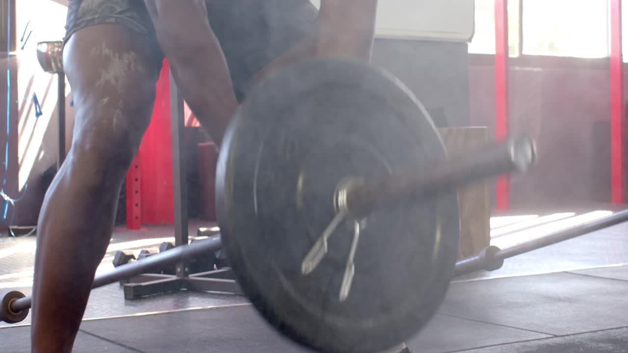 Haltérophile afro-américain prenant de la magnésie, se préparant puis soulevant une barre chargée dans une salle de sport.