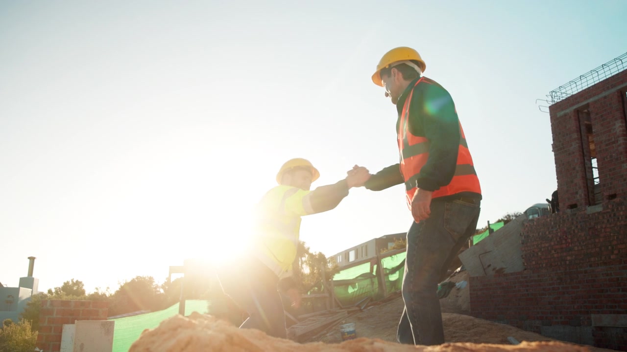 Construction Worker Helping Colleague Stand Up at Building Site