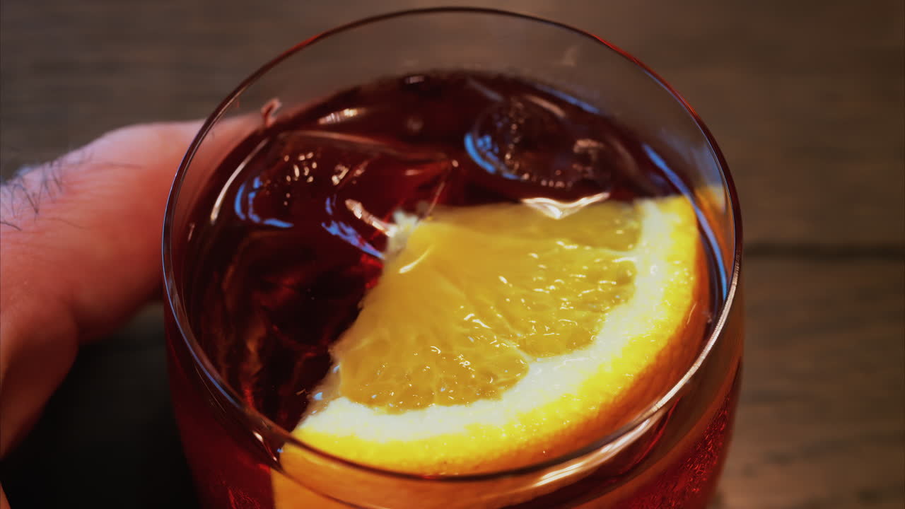 Close up of a Negroni cocktail with orange slice and ice cubes on a wooden table