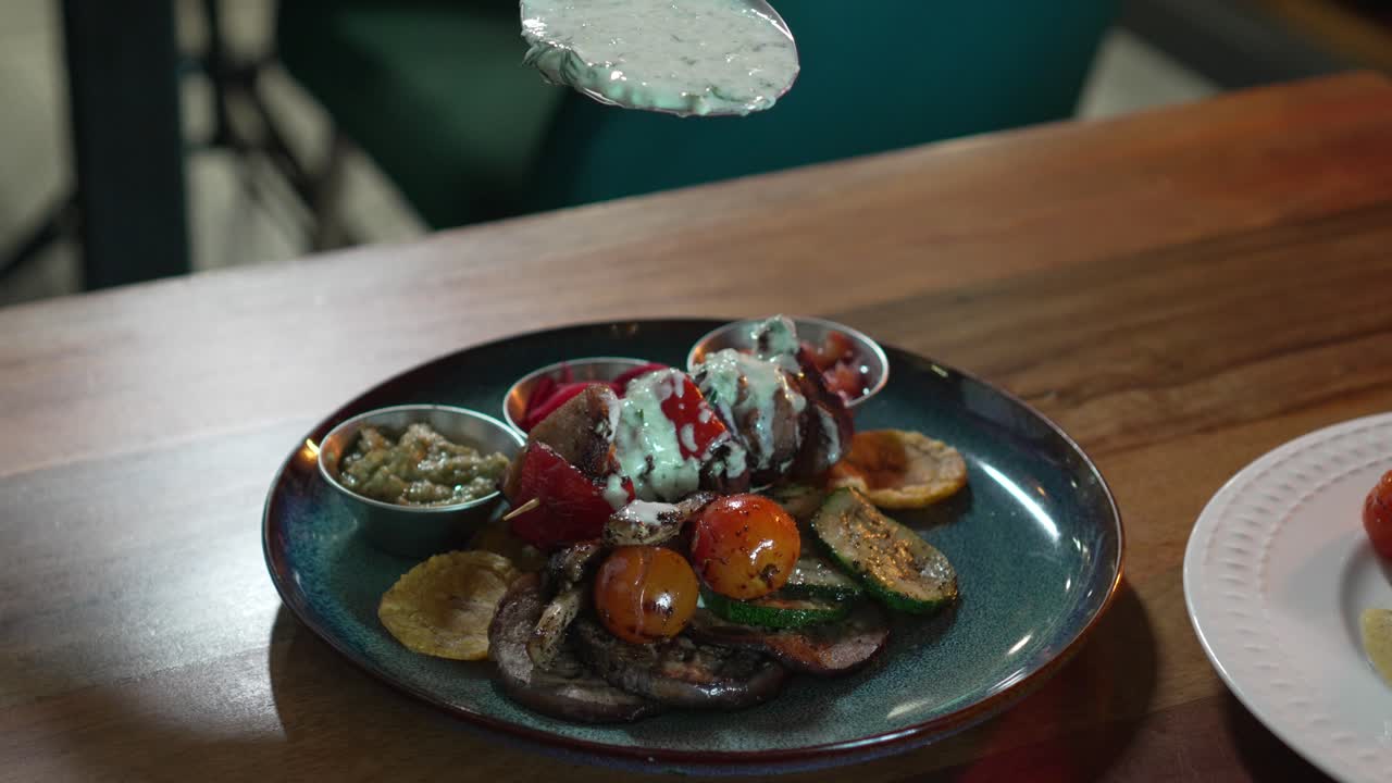 Chef pouring creamy white sauce with spoon on delicious meat plate with salad in restaurant