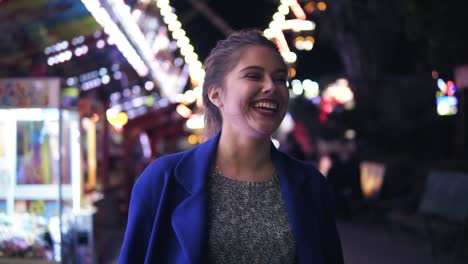 Mujer-Joven-Feliz-Caminando-En-El-Parque-De-Diversiones,-Sonriendo-Y-Riendo.-Diferentes-Atracciones-En-El-Fondo.-Tiro-En-Cámara-Lenta