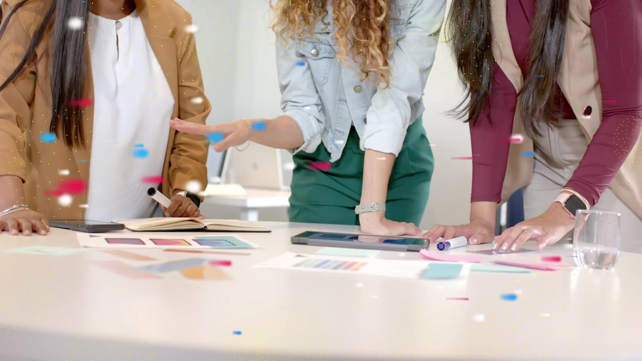 Donna leader che indica il tablet e guida il design, mentre il team tocca i colori e puntini di coriandoli fluttuano sulle mani.