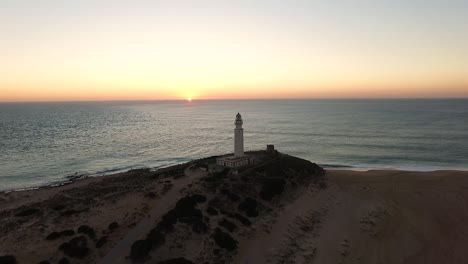 drone acercándose al faro mientras el sol se pone en las tranquilas aguas del horizonte en la costa de cádiz españa
