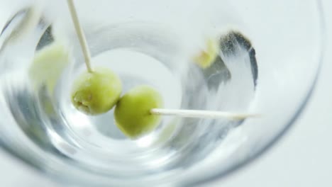 papel gris ardiendo sobre el primer plano de las aceitunas en un vaso de cóctel contra un fondo gris