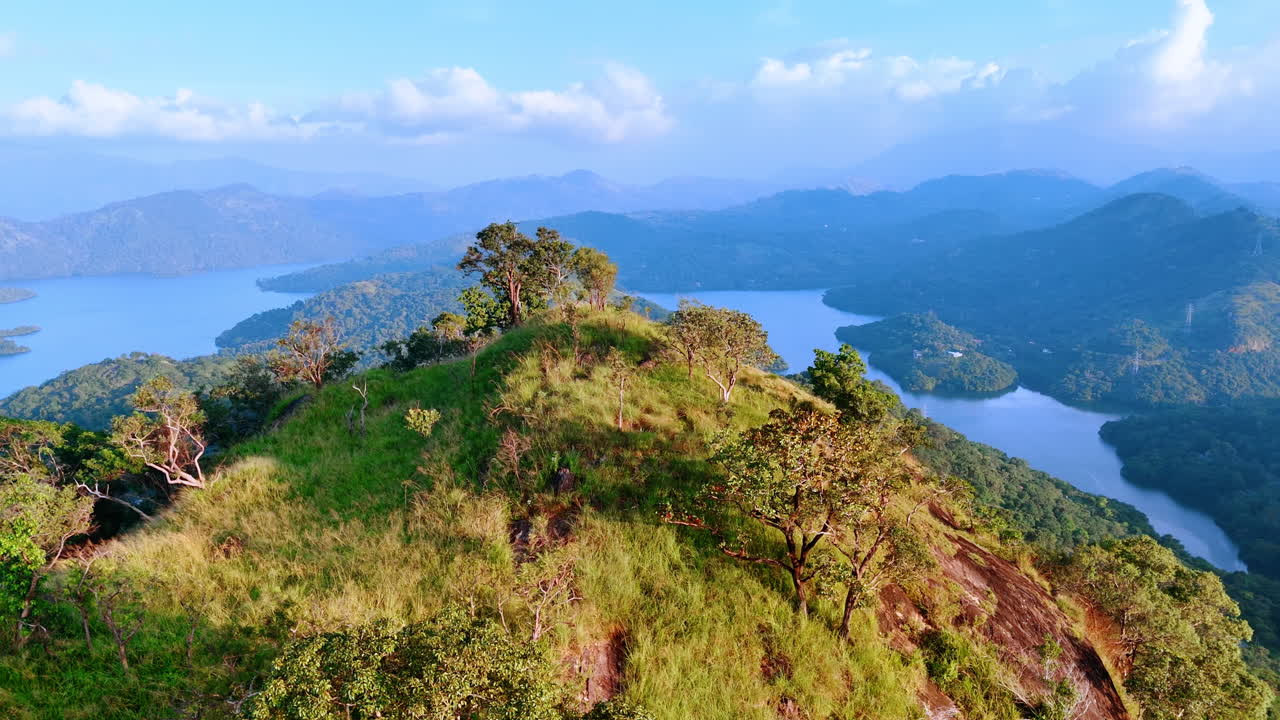 Top of the mountain covered with grass and some trees. Beautiful lakes and rocky silhouettes in the fog at backdrop.