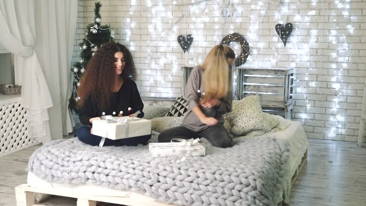 Amiche con scatola regalo a casa. Giovani donne con scatole regalo in una calda atmosfera casalinga che festeggiano il Natale.
