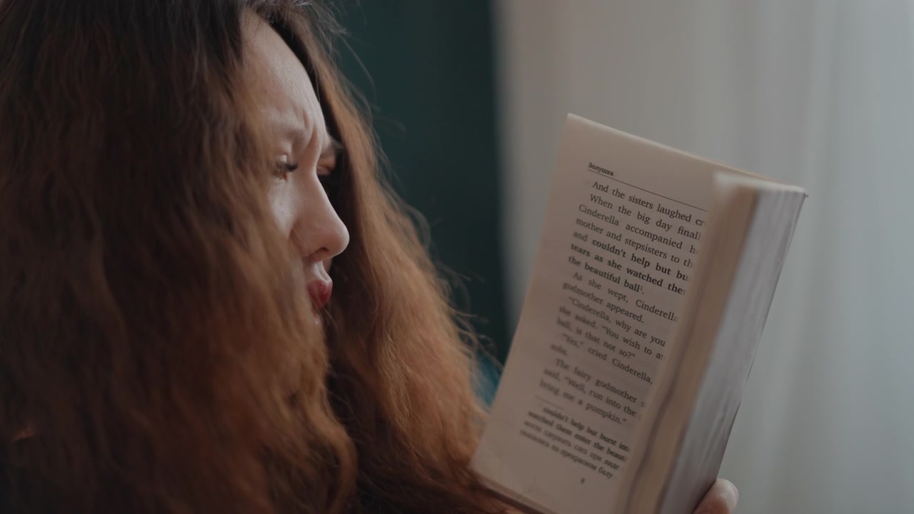 Woman with long wavy hair holds printed page upright and reads in close three-quarter profile, focused gaze and slightly parted lips showing absorption, quiet concentration, soft window light, and