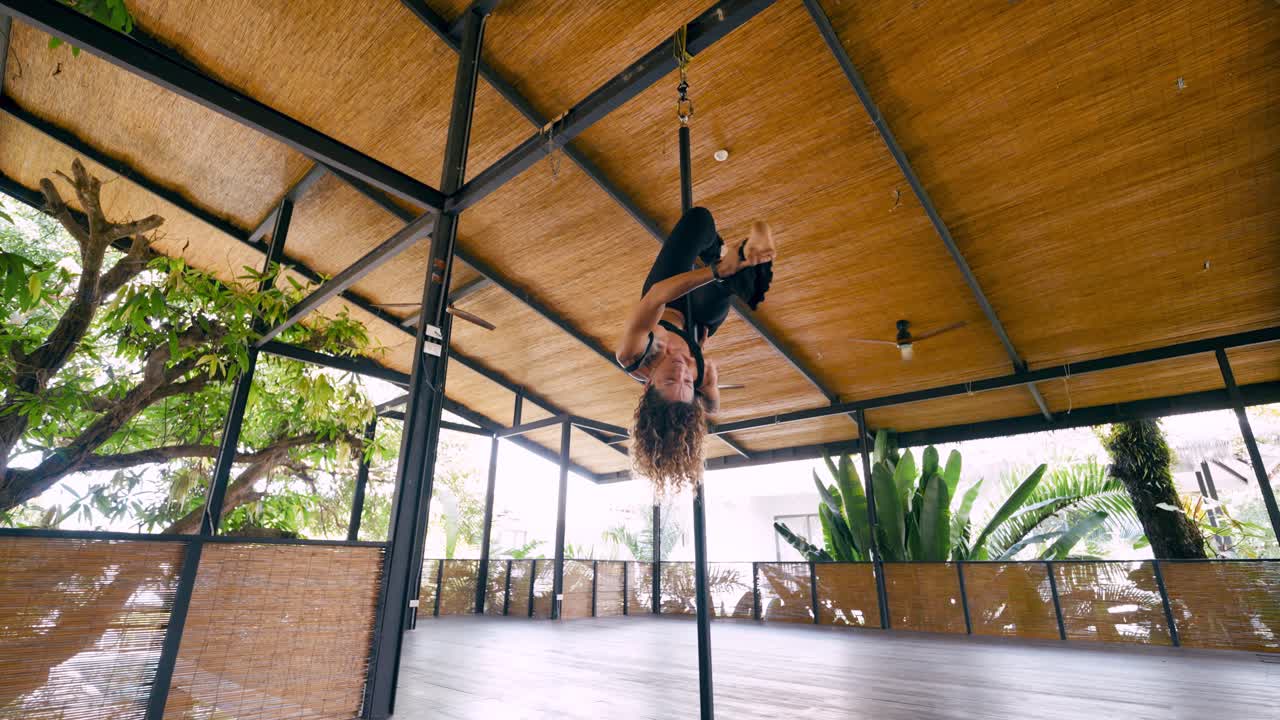 Mulher realizando pole fitness aéreo de cabeça para baixo em estúdio tropical
