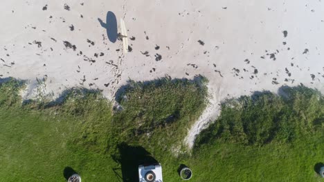 top view of a man running with his surfboard from his land rover from green grass to the beach