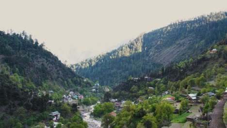 aerial drone shot of a kashmir village - a beautiful kashmir village with houses and a river surrounded by forests and mountains