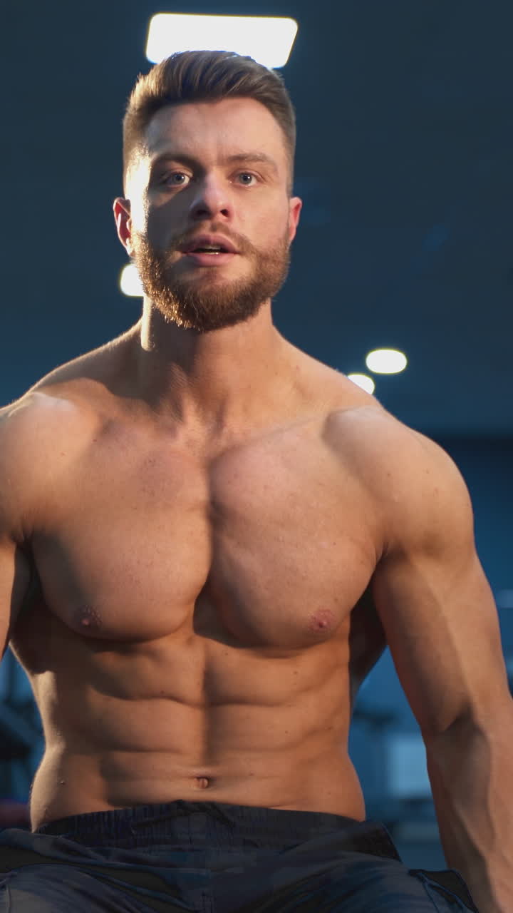 Young shirtless man training hard on the gym. Handsome bodybuilding man have a rest after training. Vertical video