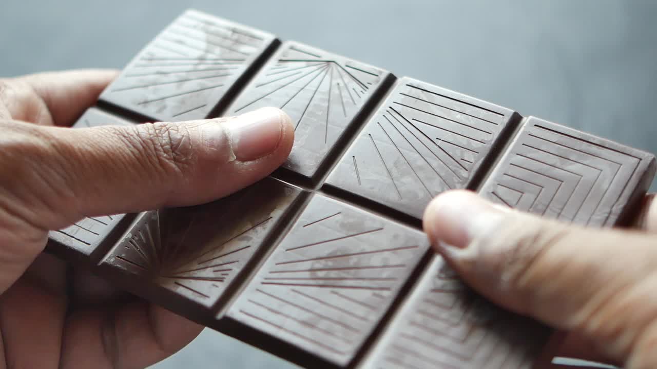 primer plano de manos sosteniendo una barra de chocolate oscuro