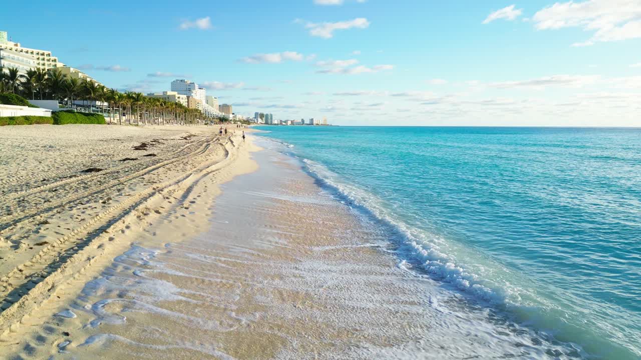 Serene beach view with gentle waves, walking people, and the Cancun skyline, playa marlyn
