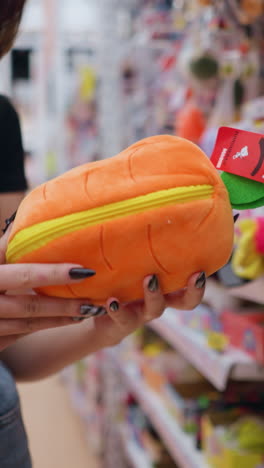 primer plano de una mano recogiendo un bolso naranja vibrante con detalles amarillos de un estante de la tienda, el comprador examina accesorios elegantes entre varios artículos empaquetados, compras minoristas de moda o productos de regalo