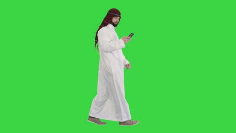 arab man using his smartphone surfing on the internet or messaging while walking on a green screen, chroma key