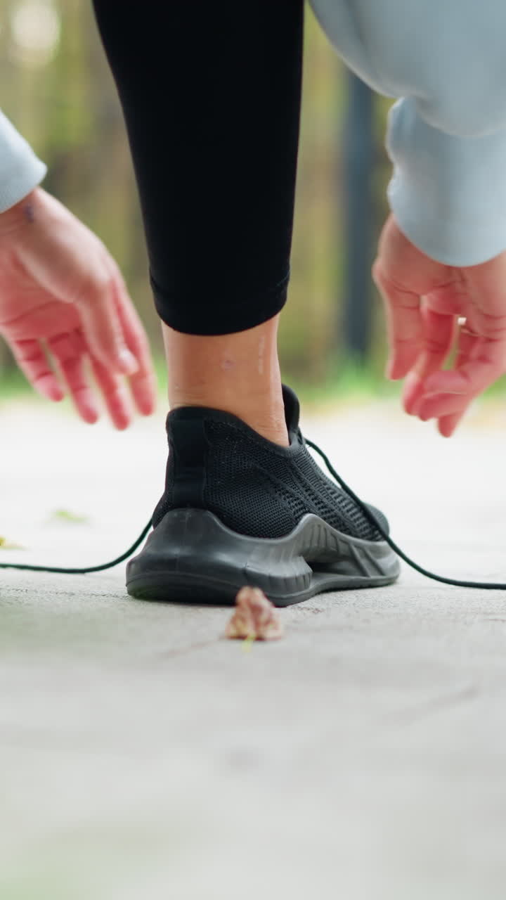 Primo piano di una ragazza in leggings neri che si allaccia la scarpa, si sta preparando per una corsa o un allenamento all'aperto, concentrandosi su fitness e preparazione atletica in un parco.