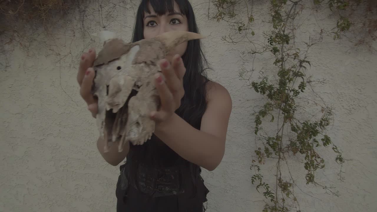 una joven bruja sostiene el cráneo de un animal con cuernos