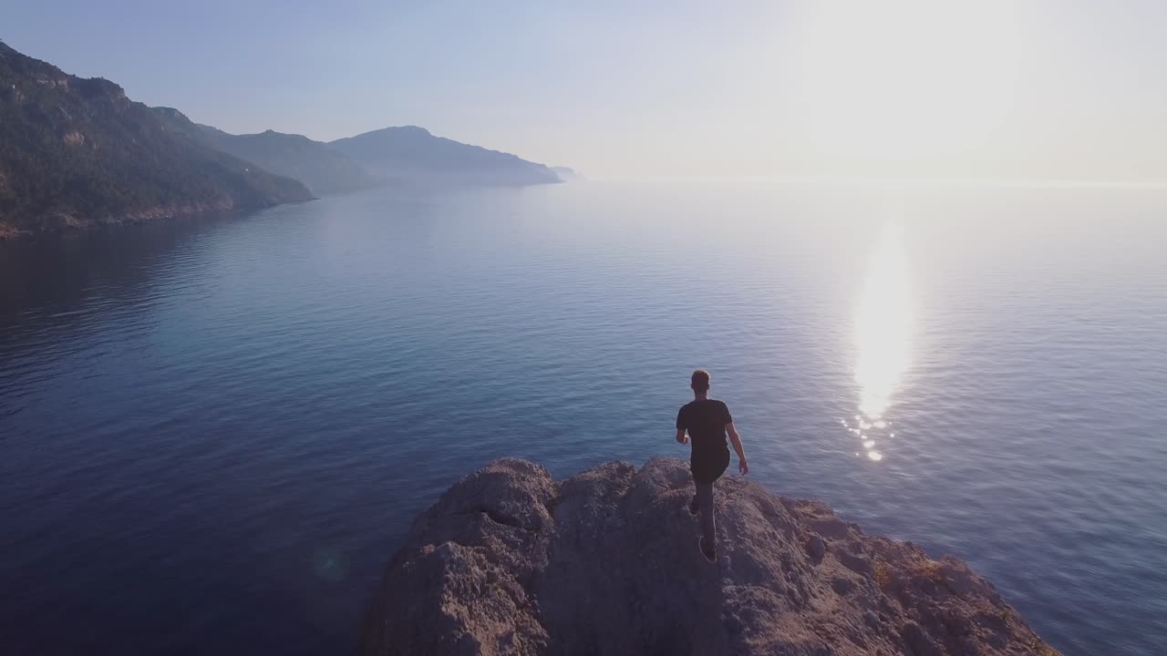 hombre caminando sobre acantilados - senderismo en las montañas - disfrutando de la vista del paisaje en el mar mediterráneo en mallorca - vista de drones de 4k - el turista de las islas baleares disfruta de la vida