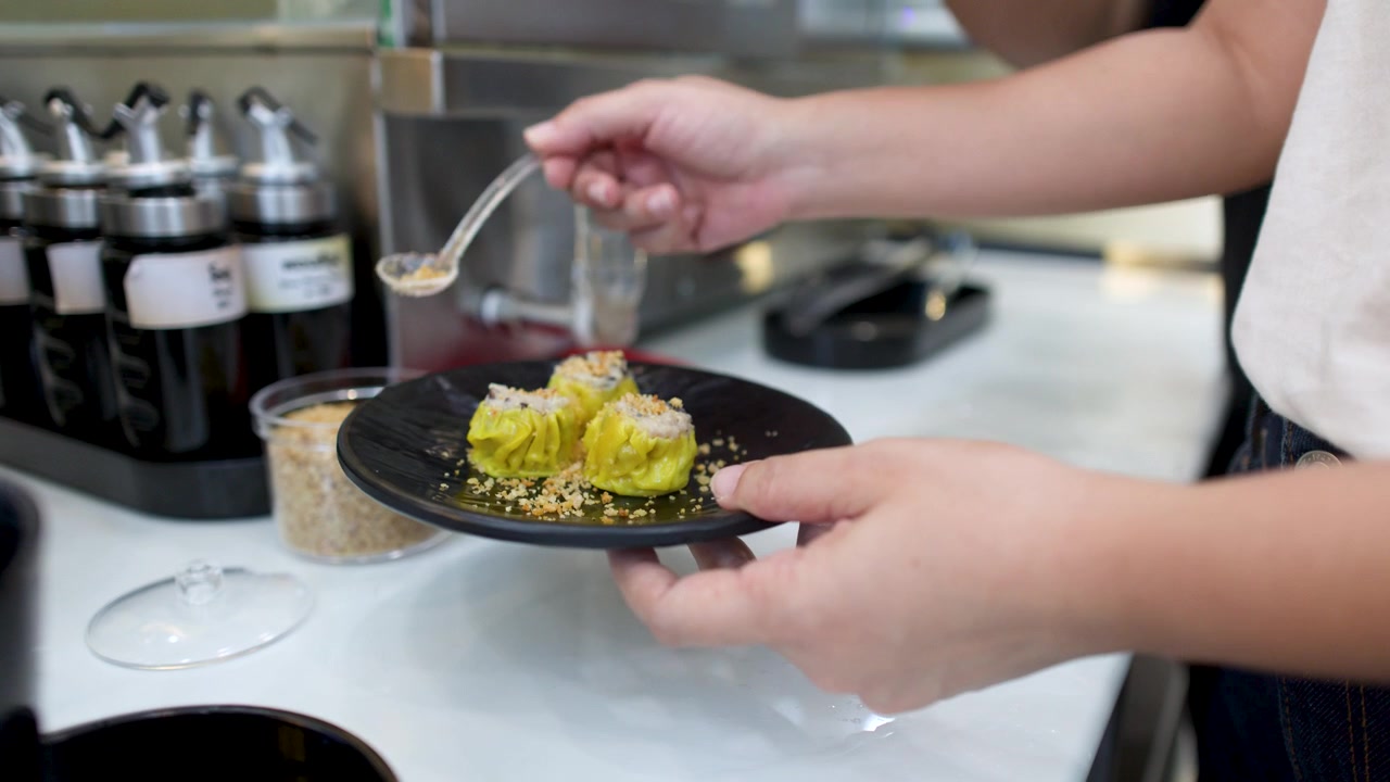 Gros plan de mains saupoudrant de l'ail frit sur des raviolis shumai jaunes à un buffet