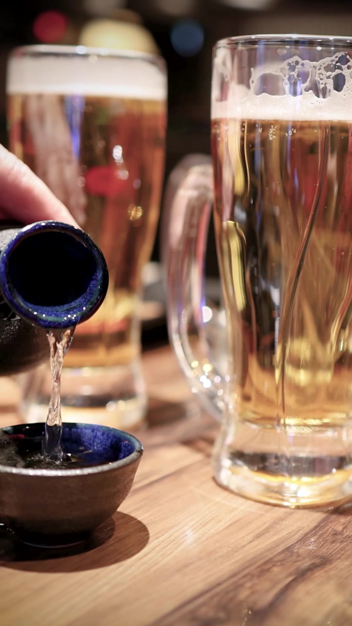 Sake versato in una piccola tazza di ceramica accanto a boccali di birra