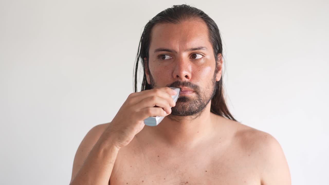 매력적인 젊은 남자가 화장실에서 거울 앞에서 면도하고 있습니다. 전기 면도기는 준비하고 있습니다.
