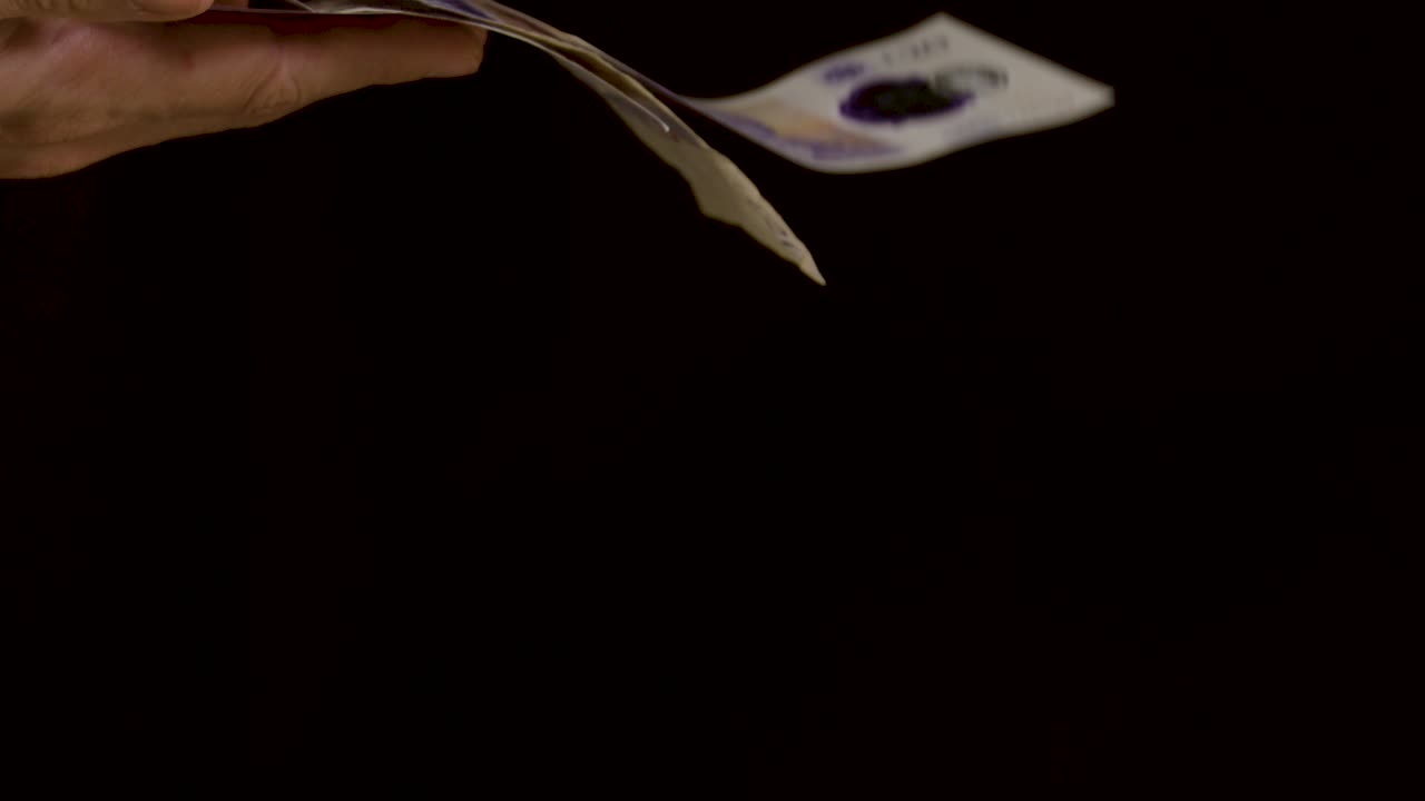 Hand spending cash money against a black background in slow motion