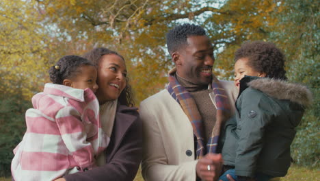 parents carrying children as family walk along track in autumn countryside