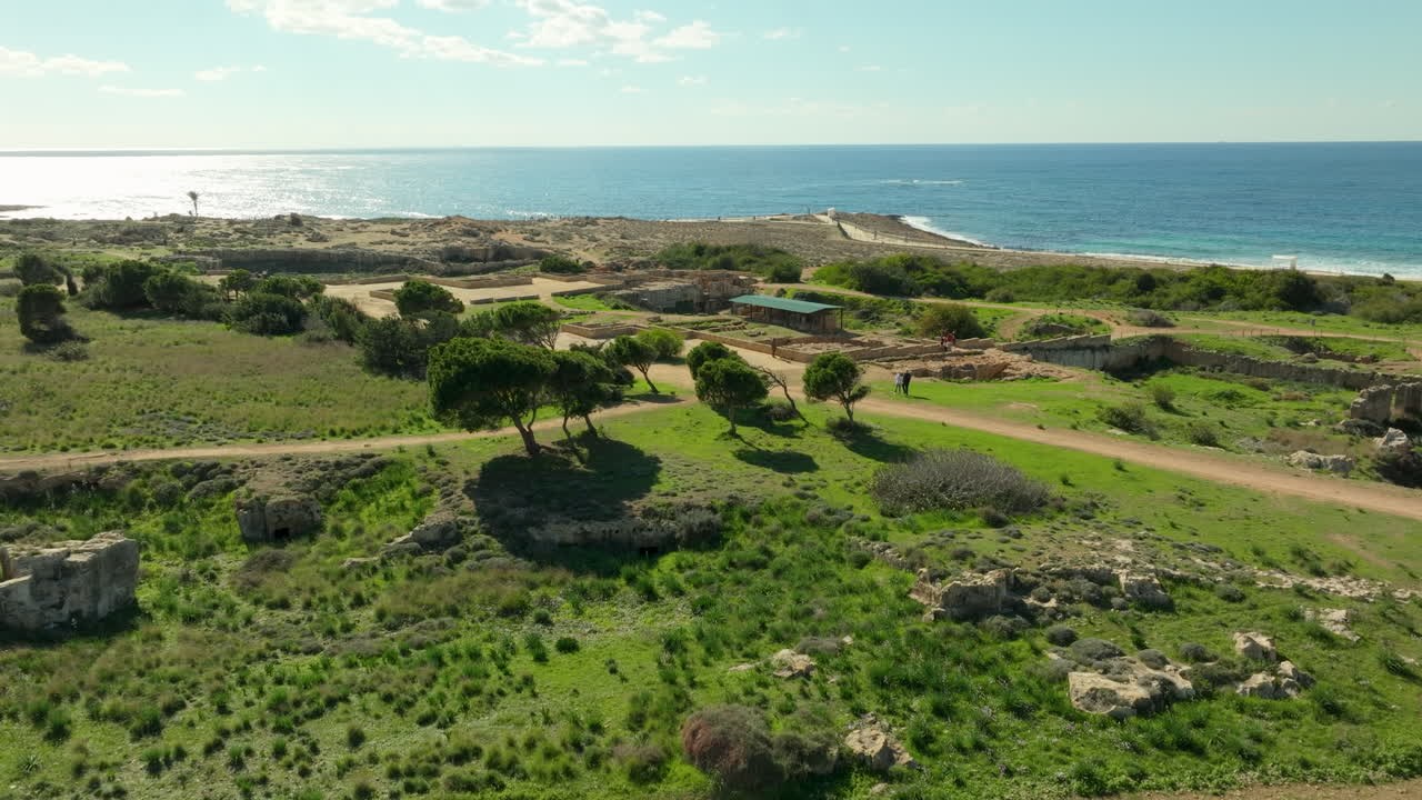 푸른 하늘 아래 지중해를 내려다보는 초록색 풍경 속에 있는 파포스의 왕들의 무덤의 역사적인 장소의 고대 폐허를 한눈에 볼 수 있습니다.