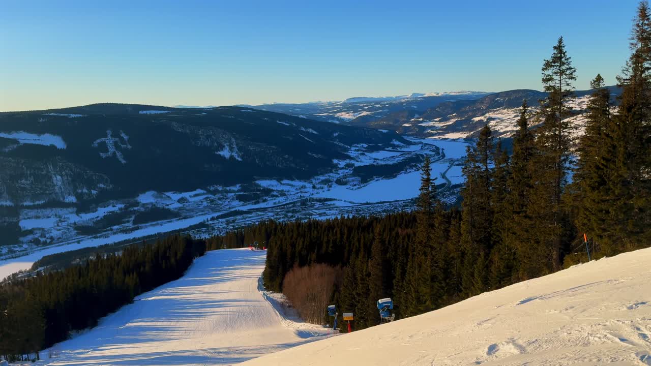 Arctic winter sunset golden hour Hafjell Alpine Resort Norway Norge Lillehammer Fakkelmannen Olympic Torch Man skiing down icy steep snow groomed trail run Øyer mountains clear sky Sjusjoen pan left
