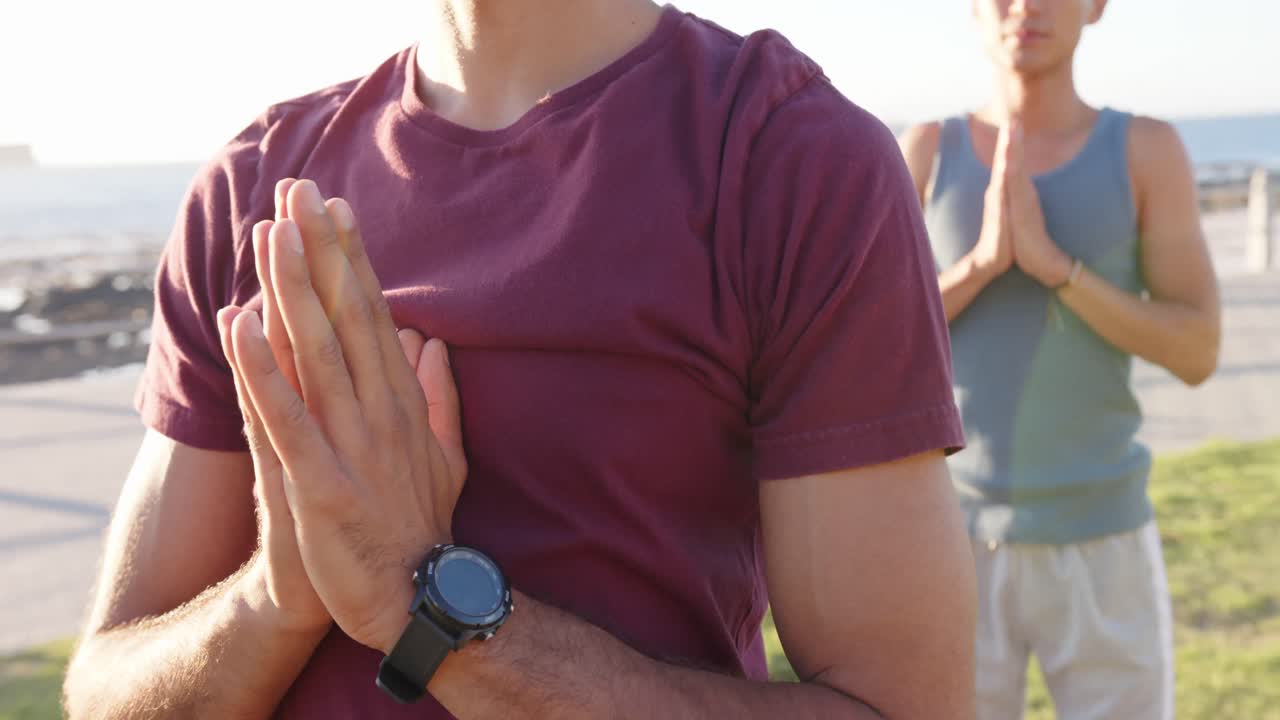 해변의 산책로에서 요가와 명상을 하는 행복한 다양한 동성애 남성 커플, 슬로우 모션