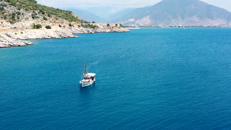 Luftdrohne-Umkreist-An-Einem-Sonnigen-Sommertag-Mit-Tropischem-Blauem-Wasser-Und-Großen-Bergen-In-Der-Ferne-Ein-Türkisches-Segelboot-In-Den-Küstengewässern-Des-Mittelmeers-In-Der-Nähe-Von-Finike,-Türkei