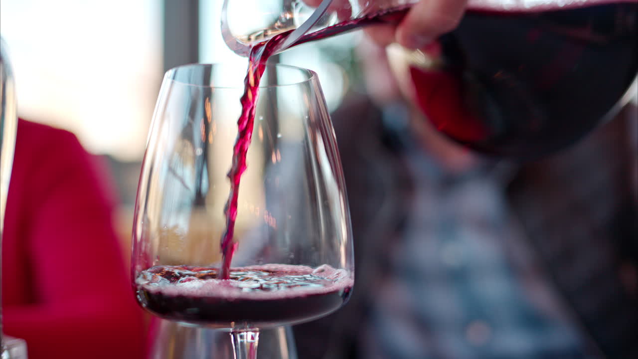 Red wine being poured in a glass at a restaurant table with blurred people on the background