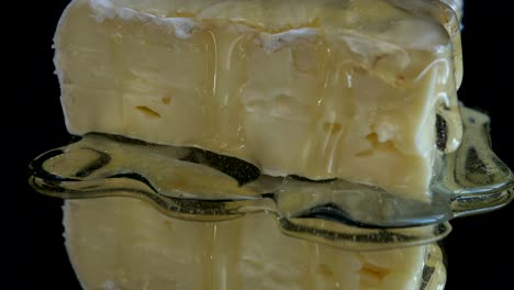 gotas de miel goteando de queso brie en un fondo negro espejado.