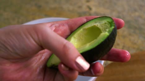 person scooping ripe avocado with a spoon in the kitchen