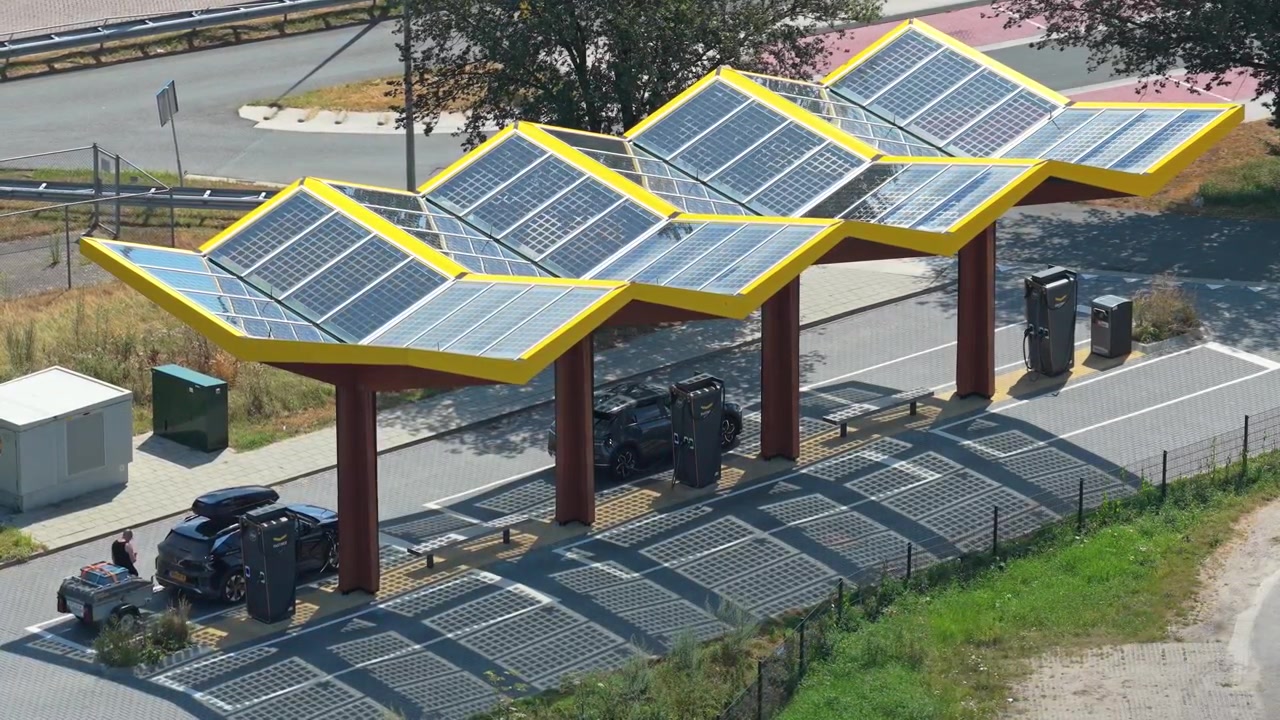 Widok z lotu ptaka na nowoczesną stację ładowania pojazdów elektrycznych z dachem pokrytym panelami słonecznymi. Samochody są zaparkowane i ładują się w centrum ładowania EV