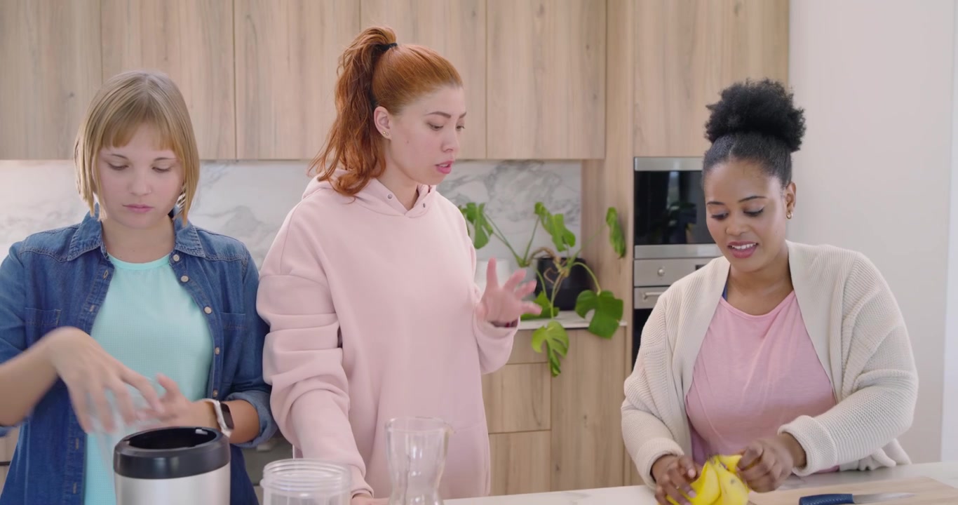 Diverse female friends prepping fruit and blender on marble island to make smoothies