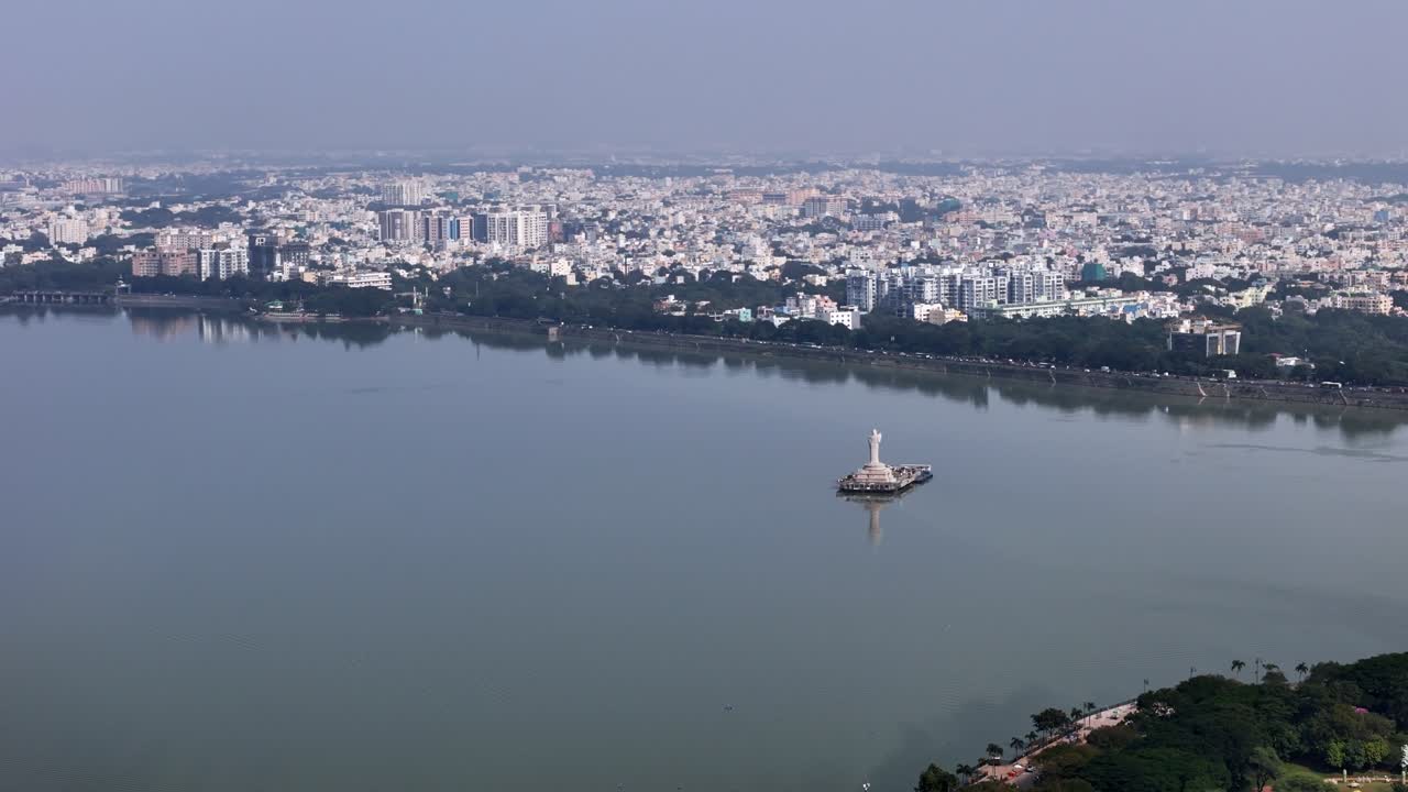 Wide aerial view of Hussain Sagar showcasing the Buddha statue island, tranquil waters, and Hyderabad’s sprawling cityscape under clear daylight. South Indian cities' residential and commercial areas