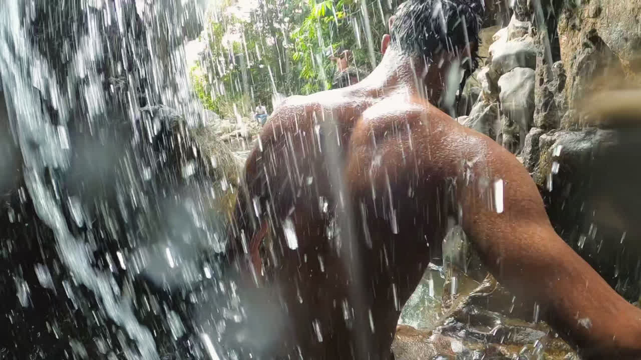 A local man is walking through a waterfall showing his body through water.