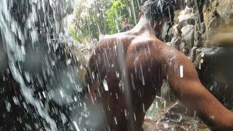 a local man is walking through a waterfall showing his body through water.