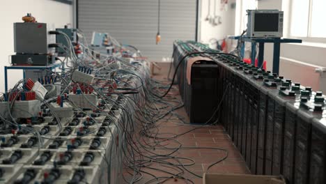 a look into a storage hall with planty of lead-acid traktion batteries with a lot of cables looking chaotic ready for controland tests