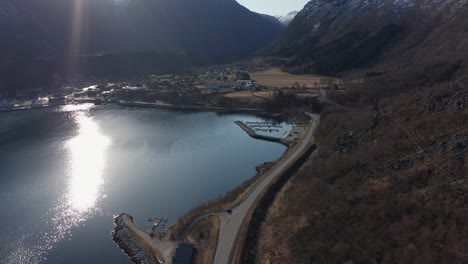 Morning-sunshine-over-Eidfjord-city-centre,-marina-and-roads---calm-idyllic-fly-in-scene---Norway