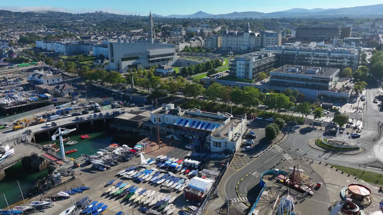 Royal St. George Yacht Club, Dún Laoghaire, County Dublin, Ireland, September 2024. Drone high angle counter clockwise orbit with moored sailboats and sweeping views of seafront buildings.