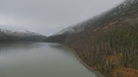 Misty-lake-in-Norway-with-autumn-foliage-and-faint-rainbow,-aerial-view