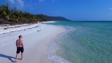 crystal clear turquoise water gently lapping against a pristine white sand beach, lined with lush palm trees and a lone tourist enjoying the serene tropical paradise. aerial view overflight drone