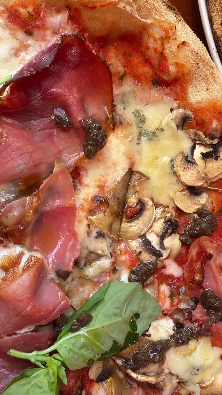 Primo piano appetitoso di una pizza gourmet con prosciutto e funghi.