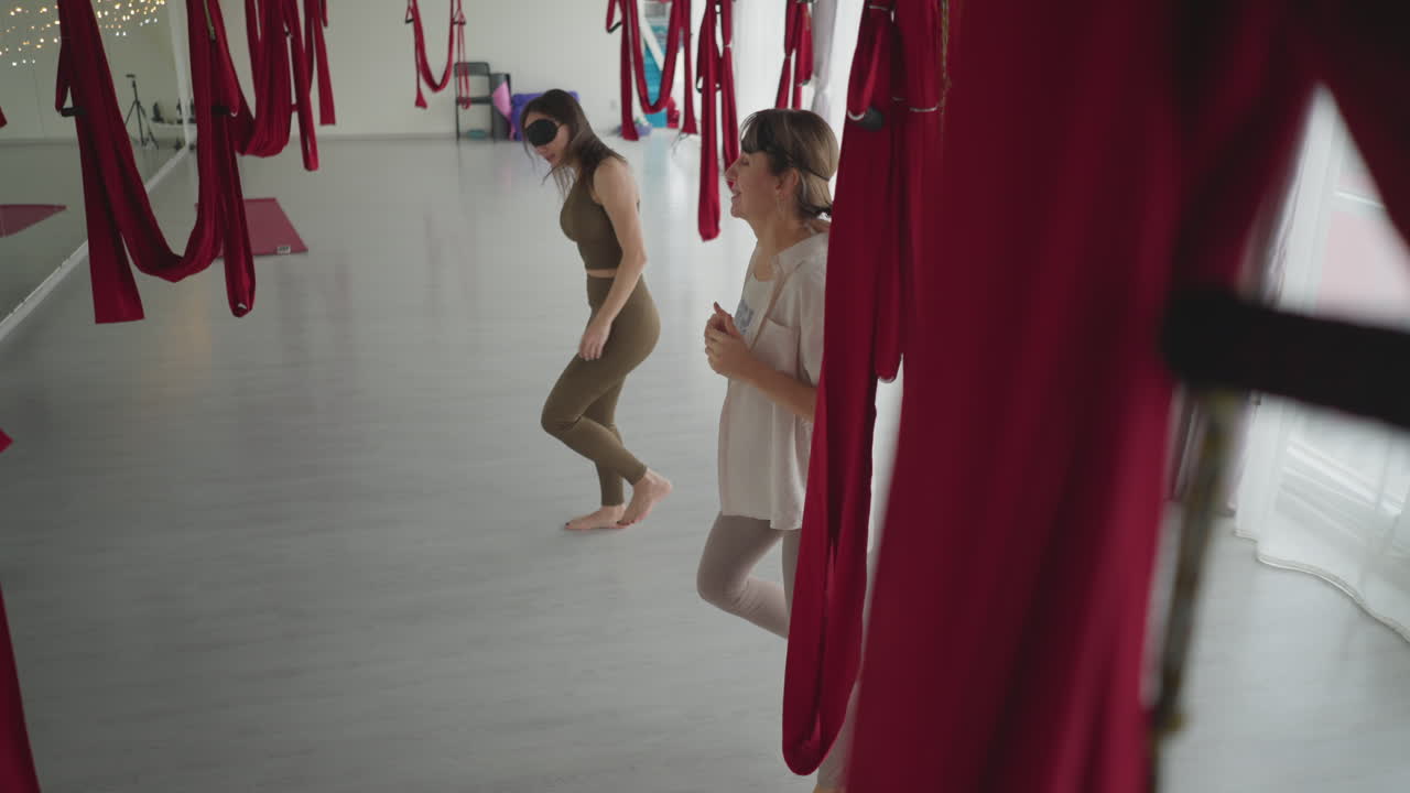Mindfulness practitioners blindfolded under red aerial hammocks shaking bodies rhythmically and clapping hands in relief practice, eyes closed, releasing tension through guided movement