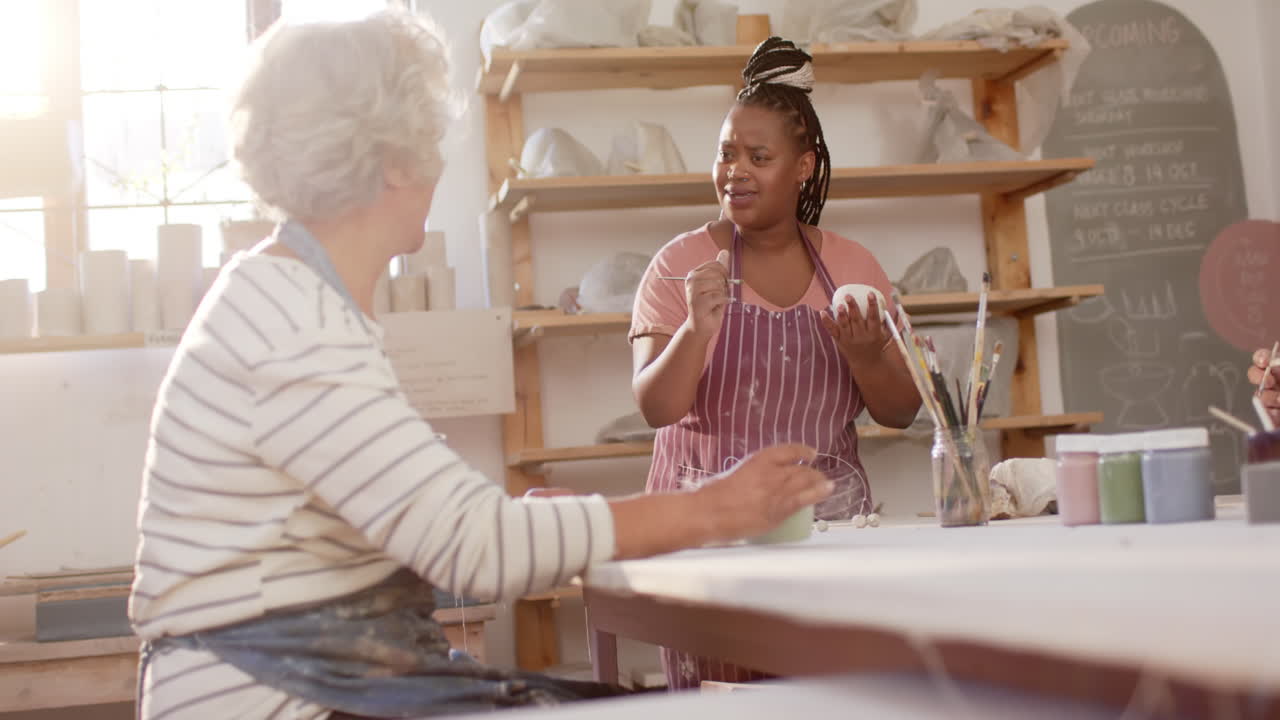 Due ceramiste diverse che lavorano e discutono in uno studio di ceramica, al rallentatore